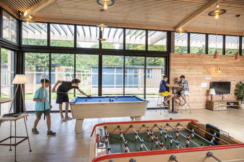 Niños juegan billar y futbolín en una sala iluminada del Camping de Paris, Île de France, Francia.