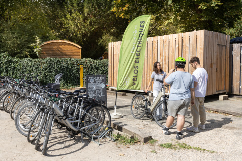 Billede af gæster, der lejer elektriske cykler ved Camping de Paris i naturskønne omgivelser.