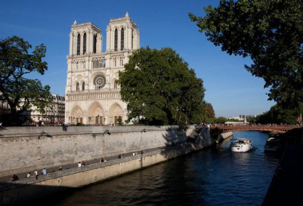 Vista de la catedral de Notre-Dame y el río Sena en París, con barco y gente sentada cerca del muelle.