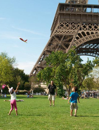 Niños juegan y vuelan aviones de juguete en el césped cerca de la Torre Eiffel en París, en un día soleado.
