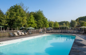 Udendørs swimmingpool med liggestole og træterrasse omgivet af frodigt grønt i Camping de Strasbourg.
