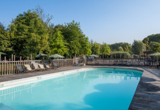 Outdoor swimming pool with sun loungers and wooden deck surrounded by trees at Camping de Strasbourg, France.
