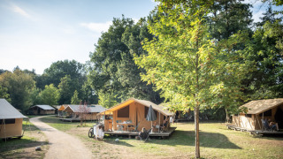 Foto di un campeggio safari Bungalow tent Classic circondato da alberi e luce solare in uno spazio verde.