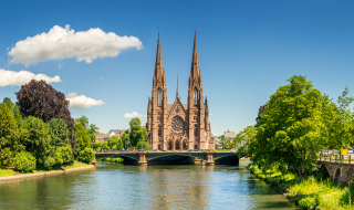 Vista panoramica di una chiesa gotica sul fiume a Strasburgo, Francia, circondata da alberi verdi.