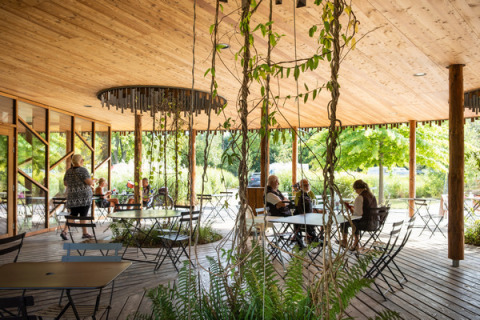 Terraza cubierta con techo de madera, plantas y personas sentadas en Camping de Strasbourg, Grand Est, Francia.