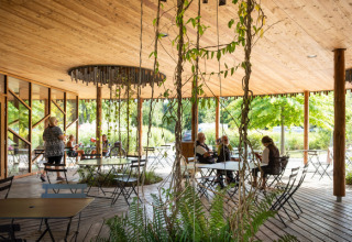 Overdekt terras met houten dak, planten en gasten bij Camping de Strasbourg, Grand Est, Frankrijk.
