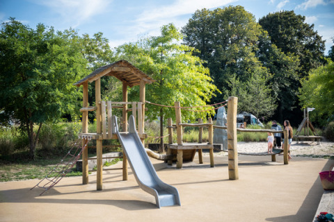 Parque infantil con tobogán y estructura para escalar en Camping de Strasbourg, rodeado de árboles y familias.