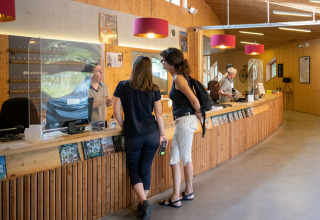 Guests talking with staff at the reception desk of Camping de Strasbourg, a holiday park in Grand Est, France.