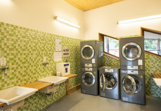 Buanderie du Camping de Strasbourg avec machines à laver, carrelage vert mosaïque et lavabos muraux.