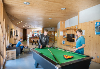 Mensen spelen biljart in een modern houten verblijf op Camping de Strasbourg, een vakantiepark in Grand Est, Frankrijk.