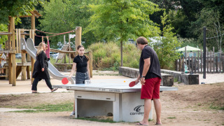 Huéspedes juegan al ping-pong al aire libre en Camping de Strasbourg, con parque infantil al fondo.
