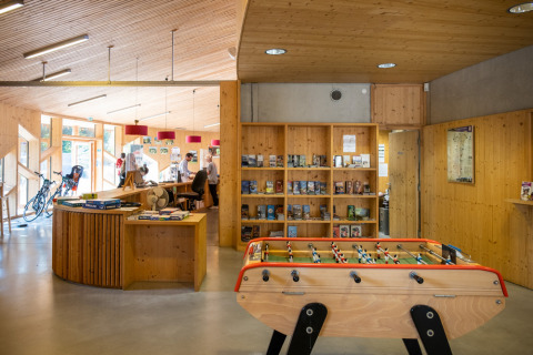 Recepción de Camping de Strasbourg con futbolín, bicicletas, mostrador y estanterías de madera con libros.