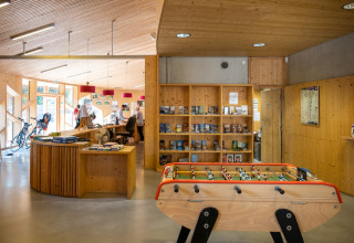 Inkomhal van Camping de Strasbourg met tafelvoetbal, receptie, fietsen en houten boekenkasten.