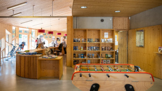 Recepción de Camping de Strasbourg con futbolín, bicicletas, mostrador y estanterías de madera con libros.