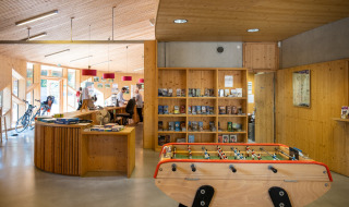 Lobby im Camping de Strasbourg mit Tischfußball, Rezeption, Fahrrädern und Bücherregalen aus Holz.