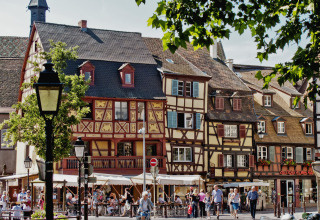 Menschen flanieren an Fachwerkhäusern und Straßencafés einer malerischen Stadt in Grand Est, Frankreich, vorbei.