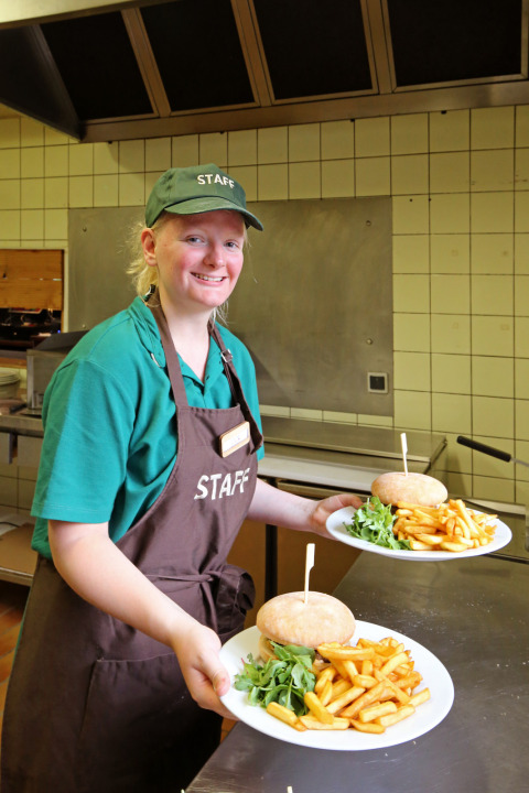 Personeelslid serveert borden met hamburgers, frietjes en sla aan Camping de l'Ill - Colmar, Frankrijk.