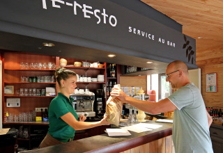 Gæst modtager mad fra personale ved café-restauranten på Camping de l'Ill - Colmar i Grand Est, Frankrig.