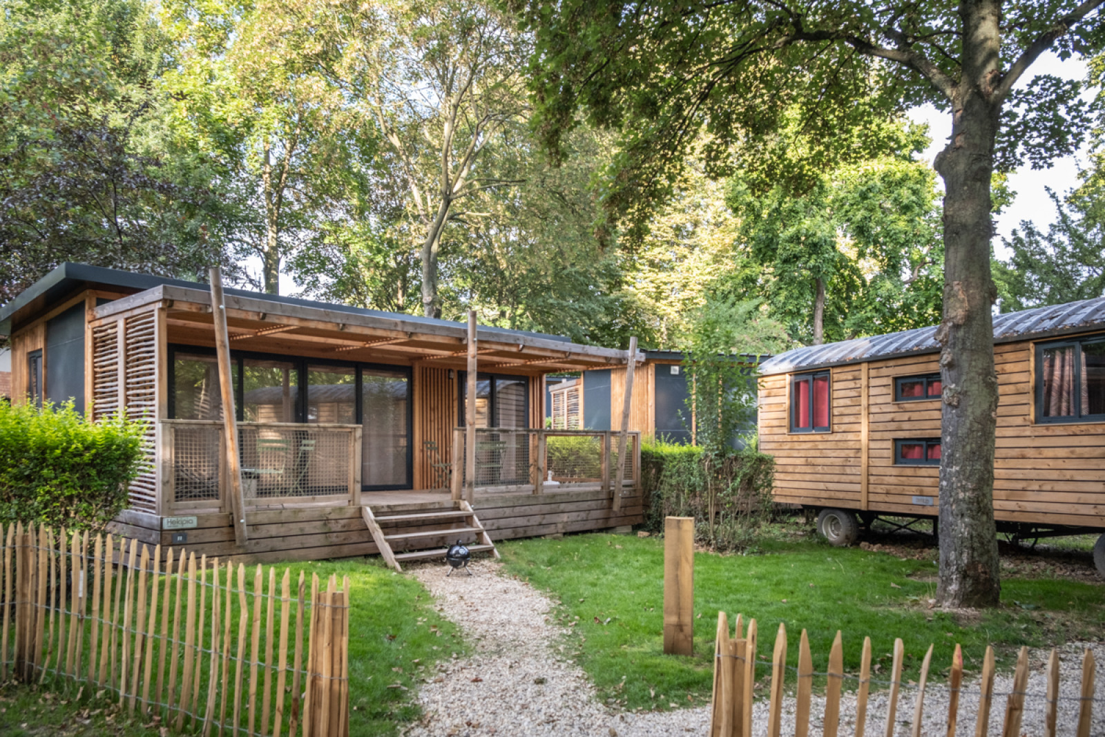 Buitenaanzicht van Chalet Evasion en caravan omringd door bomen op Camping de Paris in Frankrijk.