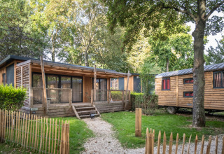 Vista exterior de la cabaña Chalet Evasion y rueda en Camping de Paris, rodeada de árboles verdes.