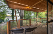 Træterrasse med borde og stole på Chalet Evasion, Camping de Paris, med udsigt til Seinen og træer.