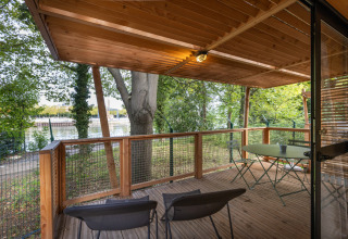 Træterrasse med borde og stole på Chalet Evasion, Camping de Paris, med udsigt til Seinen og træer.