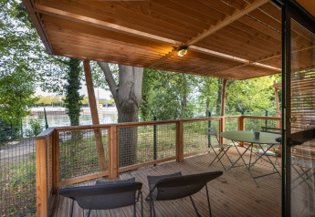 Terrasse en bois avec table et chaises au Chalet Evasion, Camping de Paris, vue sur la Seine et les arbres.