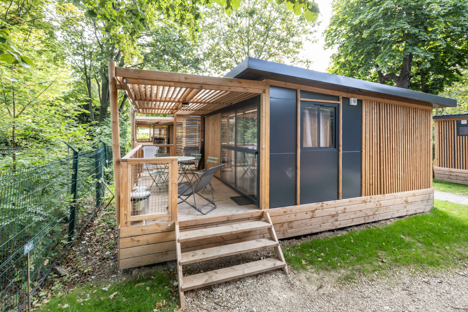 Chalet Evasion op Camping de Paris, houten terras met zitplaatsen, omgeven door bomen en natuur in Frankrijk.