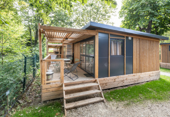 Moderne træhytte med terrasse omgivet af grønne træer på Camping de Paris, Frankrig, Chalet Evasion.