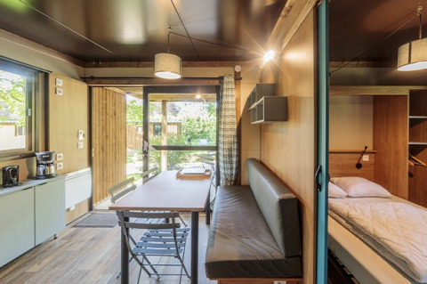 Vista interior de un acogedor alojamiento glamping Chalet Evasion con comedor, cama y cocina pequeña