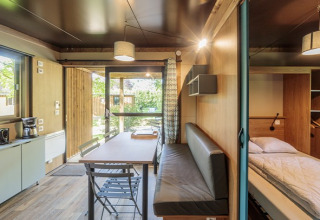 Vista interior de un acogedor alojamiento glamping Chalet Evasion con comedor, cama y cocina pequeña