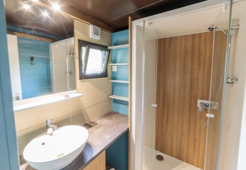 Salle de bain moderne avec douche, lavabo, étagères et fenêtre dans un chalet glamping Evasion.