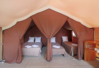Interieur van een Safari Bungalow tent Classic met drie enkele bedden, kussens, handdoeken en houten plank.