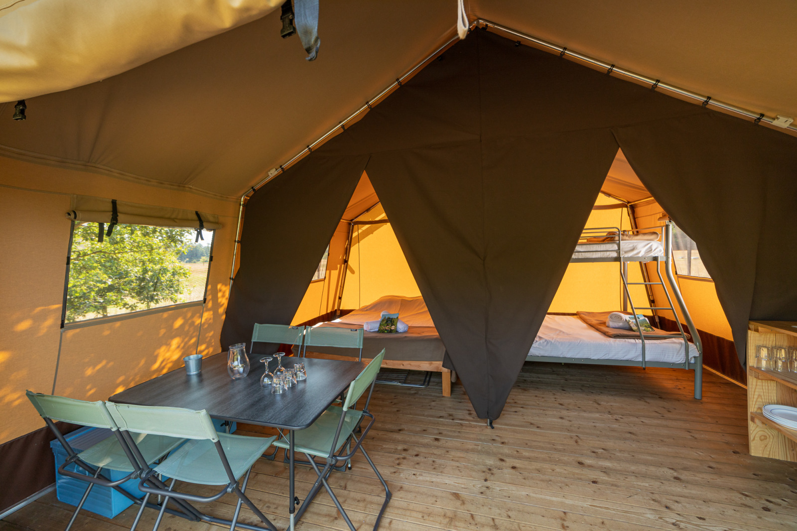 Interieur van een safaritent met eettafel, stoelen en slaapgedeelte met bedden en een stapelbed.