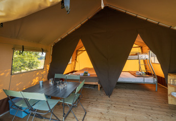 Interior de una tienda safari con mesa de comedor, sillas y zona de dormitorio con camas y litera.