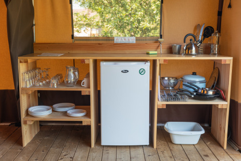 Pequeña cocina en una tienda Toile&bois Classic en Camping de Strasbourg con nevera, vajilla y utensilios.