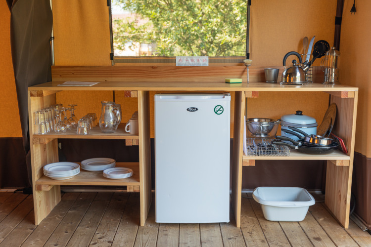 Small kitchen setup in a Toile&bois tent Classic at Camping de Strasbourg with fridge, dishes, and utensils.
