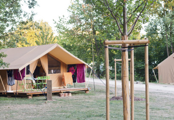Tienda safari Toile&bois Classic en Camping de Strasbourg, Francia, rodeada de árboles y sillas exteriores.