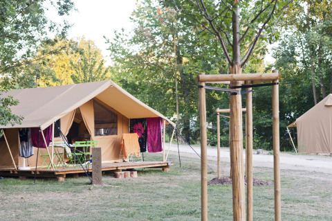 Tienda safari Toile&bois Classic en Camping de Strasbourg, Francia, rodeada de árboles y sillas exteriores.