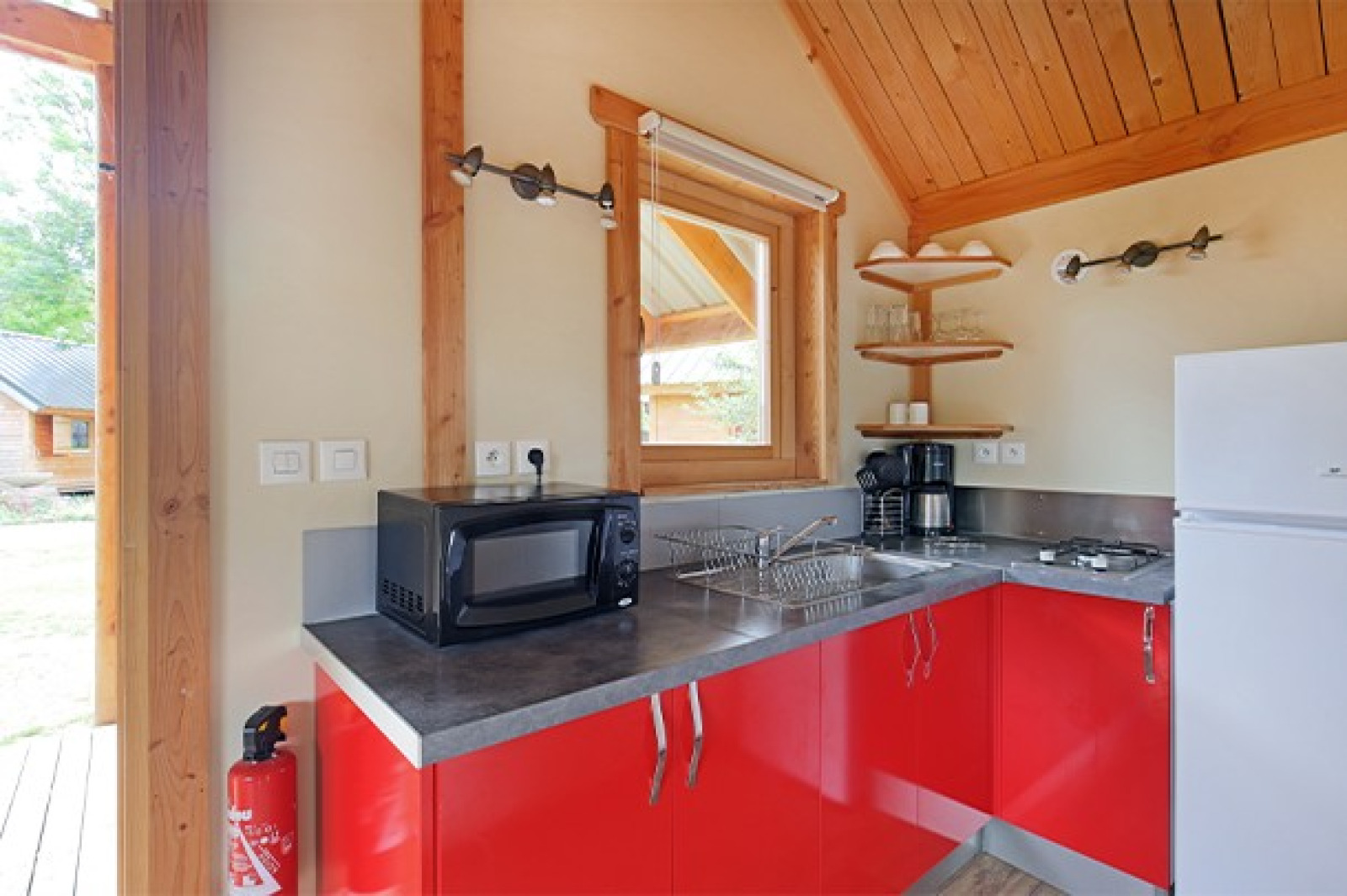 Lichte keukenhoek in Chalet Montana op Camping de Strasbourg, Frankrijk, met rode kasten en moderne apparatuur.