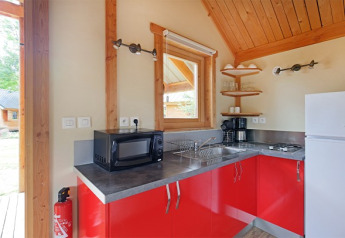 Coin cuisine lumineux dans le Chalet Montana au Camping de Strasbourg, France, avec armoires rouges et équipements modernes.