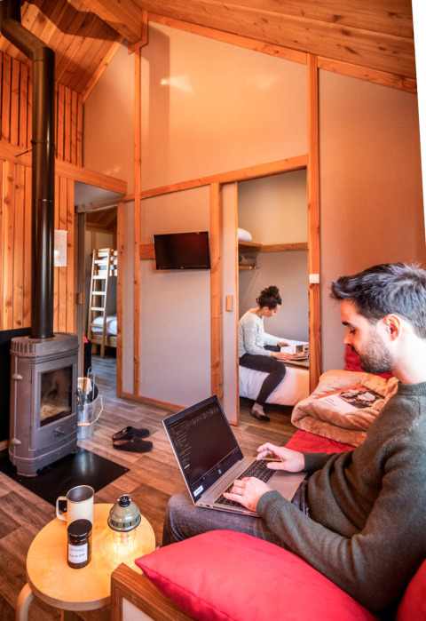 Pareja trabajando en portátiles dentro de una acogedora cabaña de madera, Chalet Montana, Camping de Strasbourg.