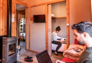 Pareja trabajando en portátiles dentro de una acogedora cabaña de madera, Chalet Montana, Camping de Strasbourg.
