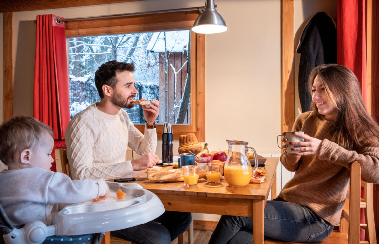 Familie genießt gemeinsam Frühstück in einer Hütte mit Blick auf verschneite Landschaft in Chalet Montana.