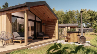 Moderne houten lodge met overdekt terras, zithoek buiten en houtgestookte hottub in een groene omgeving.