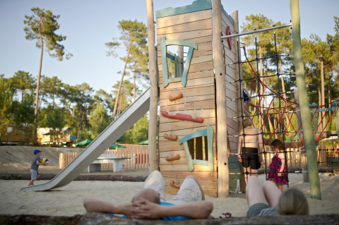 Niños juegan en un parque infantil con torre de escalada y tobogán en Huttopia Landes Sud, Francia.