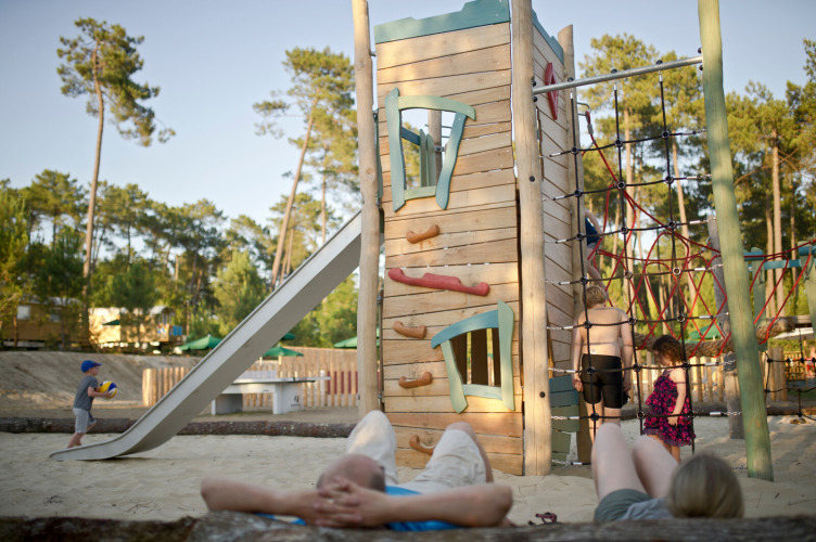 Children play on a playground with climbing tower and slide at Huttopia Landes Sud holiday park in France.