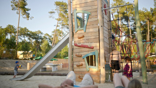 Niños juegan en un parque infantil con torre de escalada y tobogán en Huttopia Landes Sud, Francia.