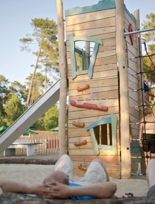 Kinder spielen auf einem Spielplatz mit Kletterturm und Rutsche im Ferienpark Huttopia Landes Sud.