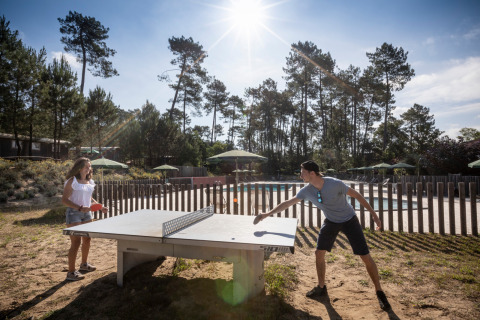 Dos personas juegan al tenis de mesa al aire libre en Huttopia Landes Sud en Nouvelle-Aquitaine, Francia.
